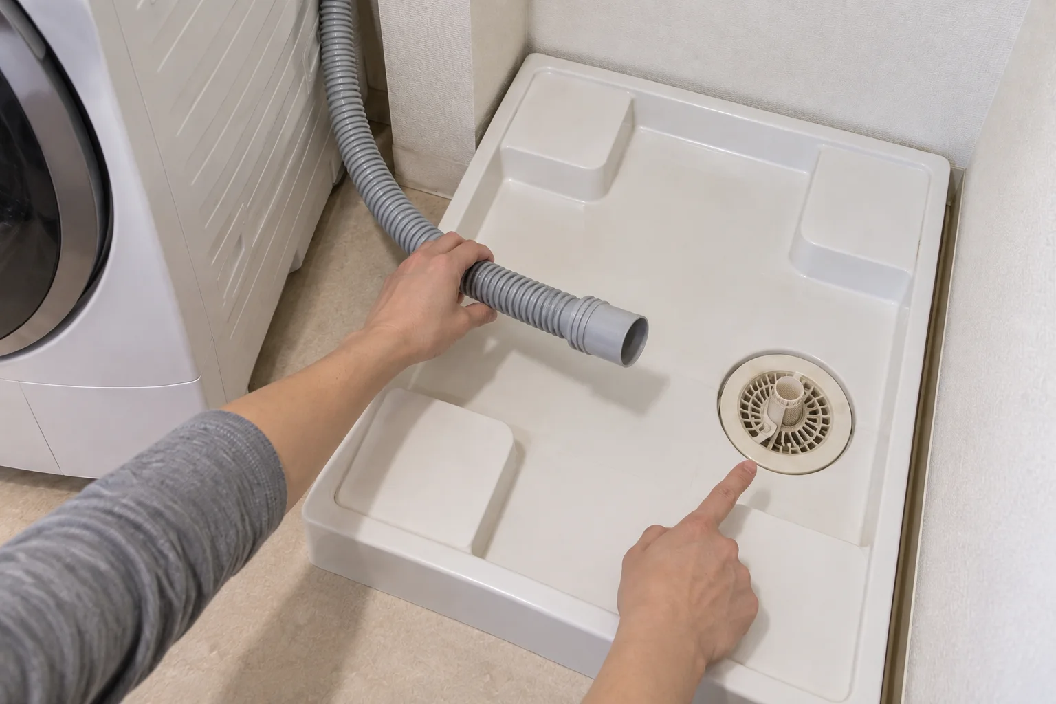 防水パン内の排水口の位置と、洗濯機から延びる排水ホースを近づけて確認している様子。